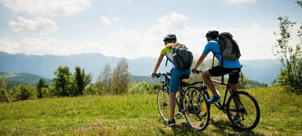 A couple riding a bicycle through a grassy field