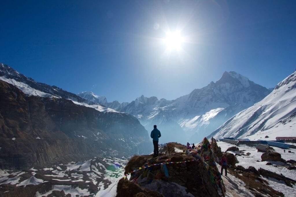 A hiker stands overlooking the majestic snowcapped Annapurna range under a clear blue sky.