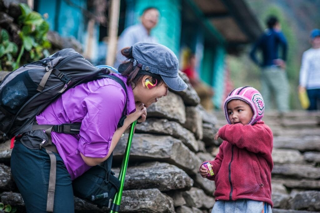 A friendly tourist interacts with a local child wearing a colorful cap in Nepal, capturing cultural connection.